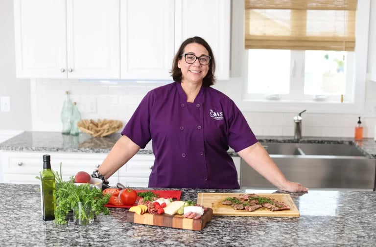 Woman in purple chefs coat smiling at kitchen counter with fresh vegetables and cooking ingredients