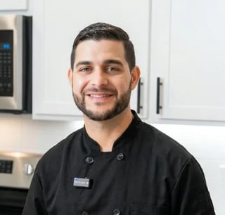 Portrait of a smiling man in a black chefs coat standing in a modern kitchen